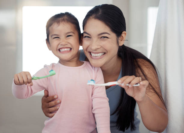 porträt von mutter und kind, die zähne putzen, zahngesundheit und reinigung im badezimmer zu hause. glückliche mutter und mädchen lernen mundpflege, wellness und frischen atem für zahnbürste, zahnpasta und lächeln - offspring child toothy smile beautiful stock-fotos und bilder