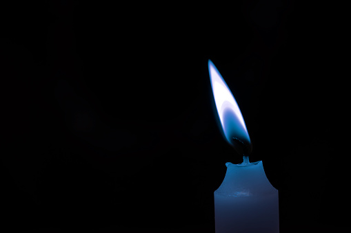 Blue  lit candle flame burning in darkness on black background.