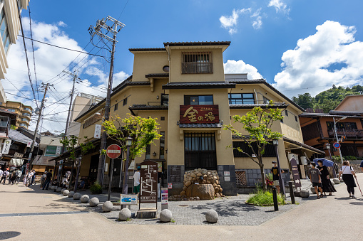 Kobe, Japan - August 18, 2022 : Pedestrians walk past the Arima Onsen hot spring ‘Kin-no-Yu’ (Gold Bath) bathing complex in Kobe, Hyogo Prefecture, Japan. Arima Onsen is a famous hot spring town.