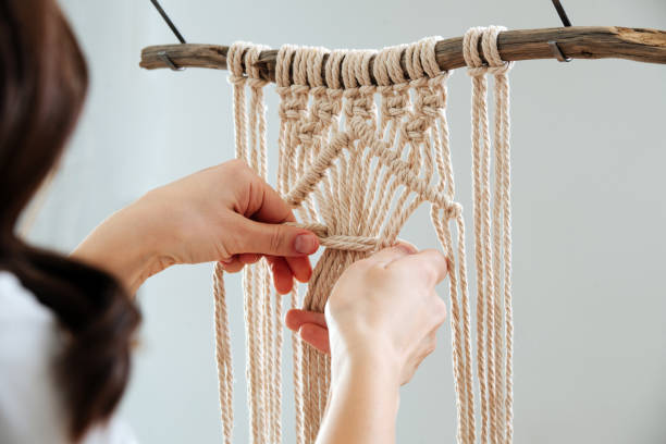 istock Woman working on a macrame piece suspended from a stick. 1441324721
