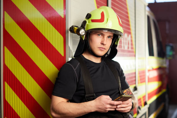 istock Portrait of a firefighter standing in front of a fire engine. Fireman using smart phone 1441326937