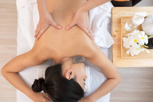 mani del massaggiatore che massaggiano la schiena della donna rilassata con olio essenziale di aromaterapia sul lettino da massaggio - massaging relaxation indoors traditional culture foto e immagini stock