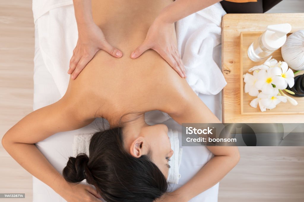 Hands of masseur massaging back of relaxed woman with aromatherapy essential oil on massage table Masseur hands make back massage with aromatherapy essential oil for young attractive woman on massage table at spa salon, top view image. Massaging Stock Photo