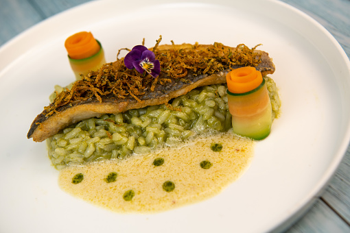 Recipe for fried fillet of sea bass with herb risotto, white wine sauce, fresch creme, roll of carrot and courgette strips, candied and fried lemon peel, High quality photo