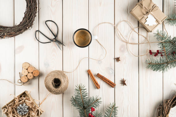 istock Handmade gift box in festive package decorated with postcard, top view. Spruce branches, cinnamon, cup of coffee and tools. Crafting present. Objects layout. Christmas or New Year holiday concept 1441329893