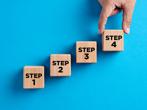 Step by step progress in business planning, career improvement or problem solving concept. Hand arranges numbers of steps with arrows on wooden cubes.