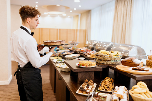 Waiter setting up food on a buffet table at hotel or restaurant