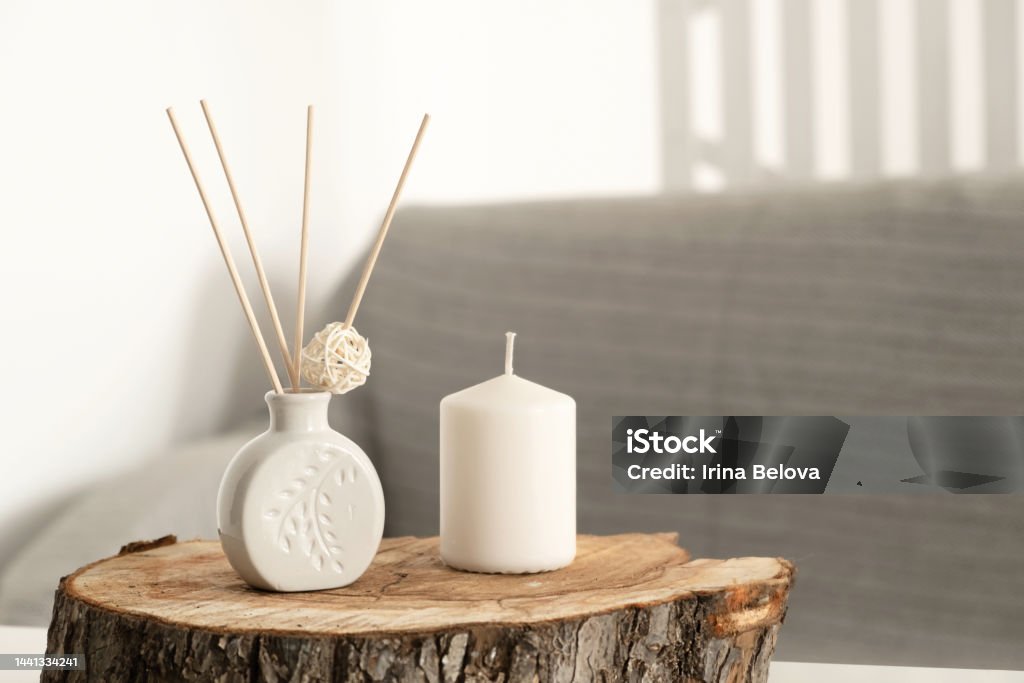 Incense sticks in aroma diffuser and white scented candle on wooden stand on table in living room. Aromatherapy, home fragrance. Concept of home relaxation and anti stress, hugge. Incense sticks in aroma diffuser and white scented candle on wooden stand on table in living room. Aromatherapy, home fragrance. Concept of home relaxation and anti stress, hugge Candle Stock Photo