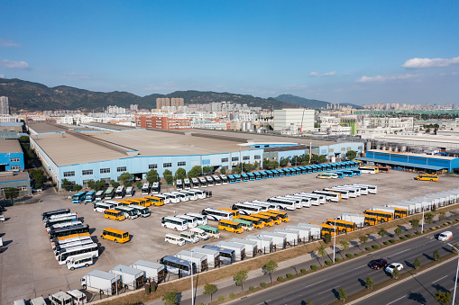 Next to the car factory under the blue sky and white clouds, new energy electric buses are parked