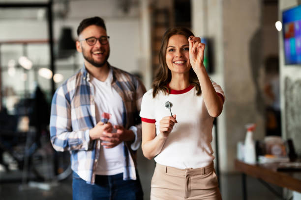 Happy young businessman and businesswoman playing darts in the office. stock photo