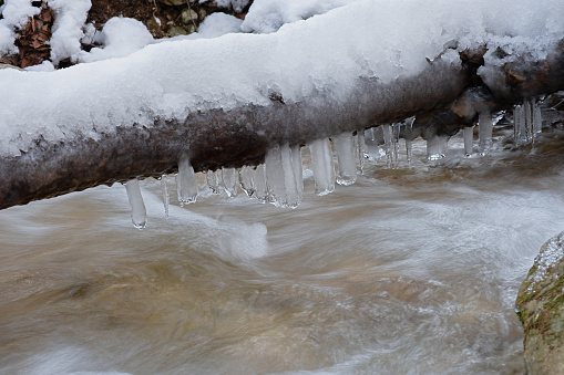 Frozen icicle river close-up. The rapid flow of the cold purest mountain river rushes over the stones. The concept of winter, cold weather, and spring snowmelt. Natural authentic neutral background