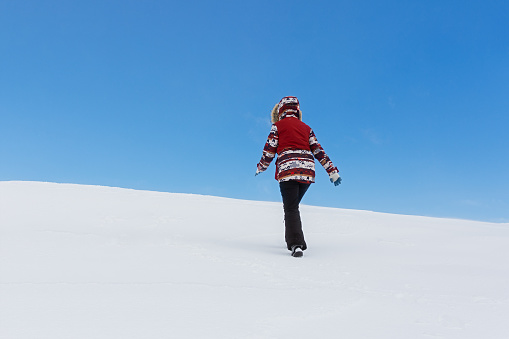 Snowy landscape of a tourist. A winter fairy tale with snow-covered Christmas trees. A woman in a multicolored jacket climbs a mountain against a blue sky. The concept of adventure, active lifestyle