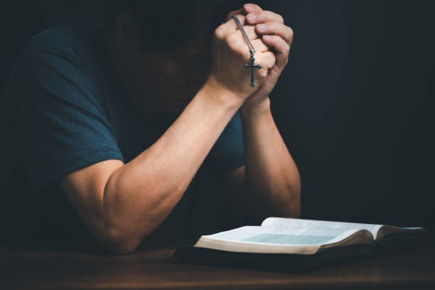 istock Man reading holy bible book and folding hands pray to God. 1441339955