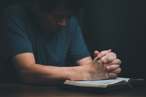 Man reading holy bible book and folding hands pray to God.