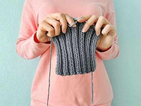 Woman knitting a gray scarf. Close up view of knitting. Needlework hobbies.