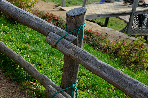 fencing of the pasture from rough-hewn logs. the connection to the post is made using a rope. the rope holds the beams through the drilled hole. simple bush craft solution without nails