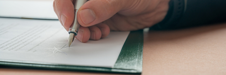Low angle closeup view of casucasian male hand signing a document or contract with an ink pen. Wide view image.