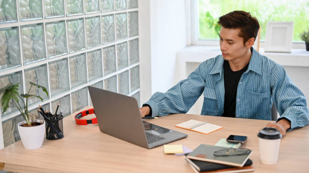 istock Handsome Asian male programmer or freelancer works on his project on laptop computer. 1441347139
