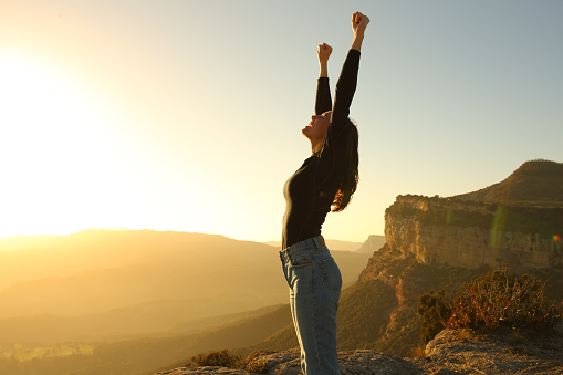 Euphoric woman raising arms in the mountain at sunset