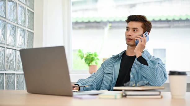 istock Professional Asian male office employee talking on the phone with his client while working 1441350336