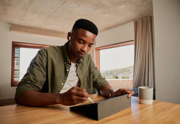 젊은 성인 흑인 아프리카계 미국인 남성이 아파트에서 원격으로 작업하는 동안 전자 태블릿에 펜으로 글을 쓰고 있습니다. 디지털 방식으로 설명하고 그리기. - ewan 뉴스 사진 이미지
