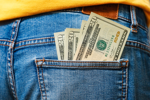 Twenty-dollar bills sticking out of the back pocket of jeans, close-up, rear view. The concept of wages, savings and wealth