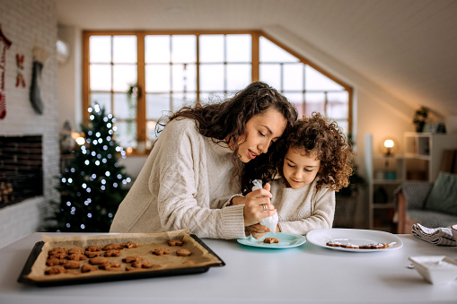 Mother and cute little daughter decorating christmas cookies together