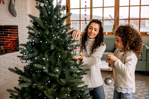 Mother and daughter decorating christmas tree in their apartment