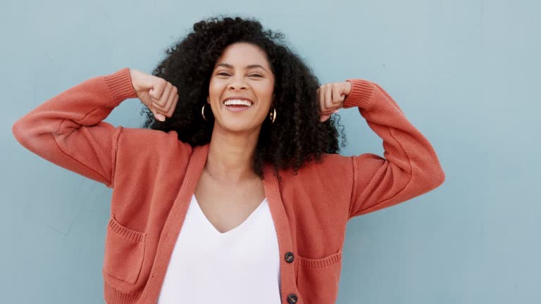 Strong, muscle and bicep with a woman flexing her muscles on a gray background or wall with mockup. Happy, smile and joke with a carefree young female having fun and laughing with a positive attitude