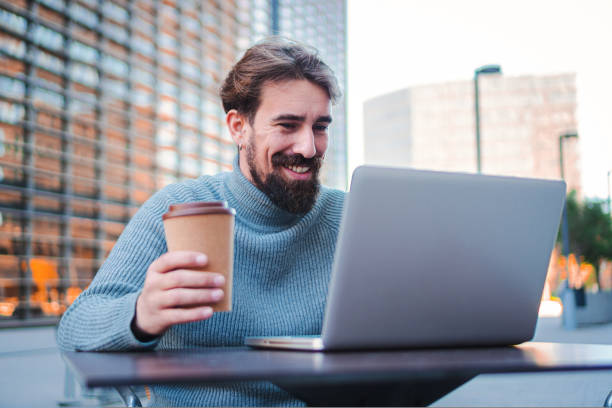 istock Happy entrepreneur man smiling and working online with a laptop computer, taking a coffee outdoors in a city terrace. Business Concept. 1441358994