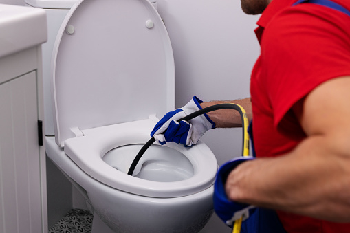 plumber unclogging blocked toilet with hydro jetting at home bathroom. sewer cleaning service