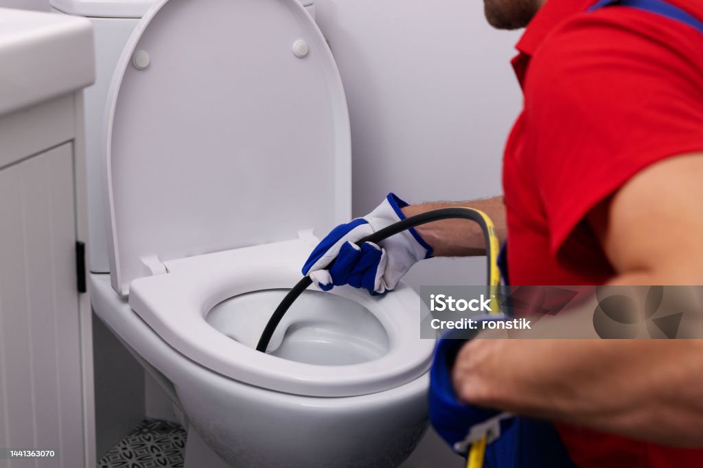 plumber unclogging blocked toilet with hydro jetting at home bathroom. sewer cleaning service Plumber Stock Photo