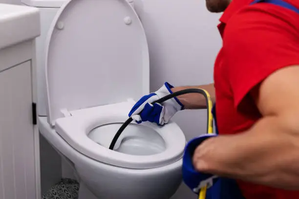 Photo of plumber unclogging blocked toilet with hydro jetting at home bathroom. sewer cleaning service