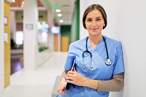 Two Female Nurses Standing In A Hospital Corridor In Uniform Smiling