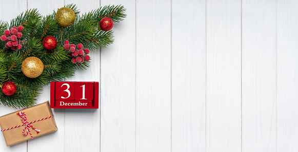 Christmas tree branch with decor, gift box and red perpetual calendar with date 31 december on white wooden background. Top view, flat lay with copy space, banner, header, New Year background