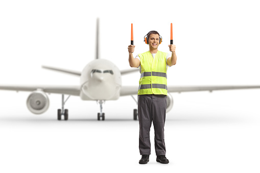 Aircraft marshaller signaling with wands in front of an aircraft at an airport apron