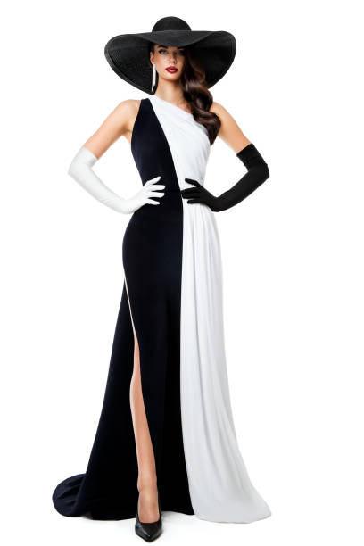女性の白黒のフォーマルドレス。長いイブニングコントラストガウンのファッションモデル。分離型背景に黒い帽子と手袋をした優雅な女性。チェスクイーンコンセプト - leg split ストックフォトと画像
