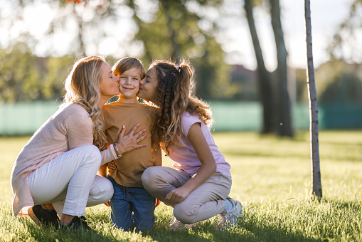 Happy mother and daughter kissing cute boy in nature