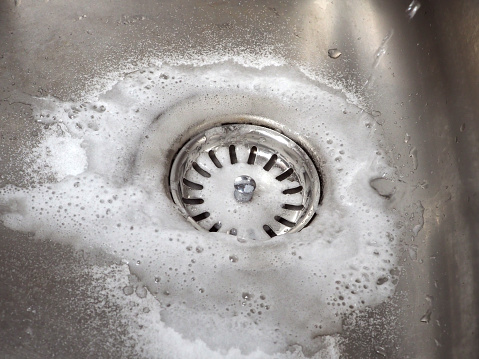 Sink drain cleaning process using baking soda and white vinegar. Close-up of a stainless steel kitchen sink. Tips for home eco-cleaning.
