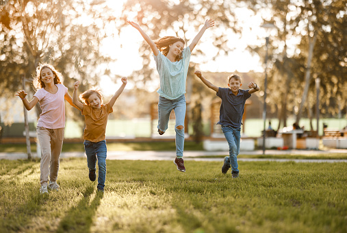 Full length of group of happy boys and girls running on the meadow during spring day