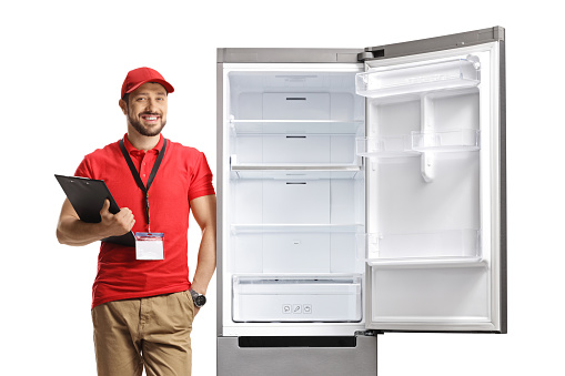 Male shop assistant leaning on a fridge and holding a clipboard isolated on white background