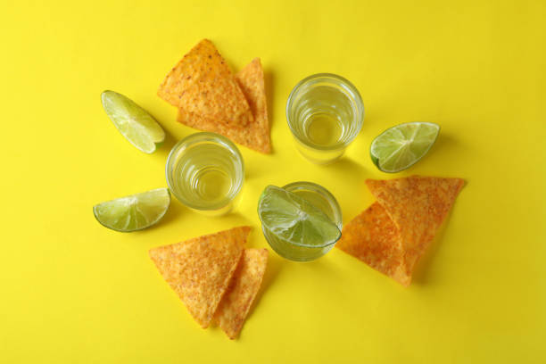 A knife next to lemon slices and eight shots of tasty tequila on a wooden cutting board - Close-up