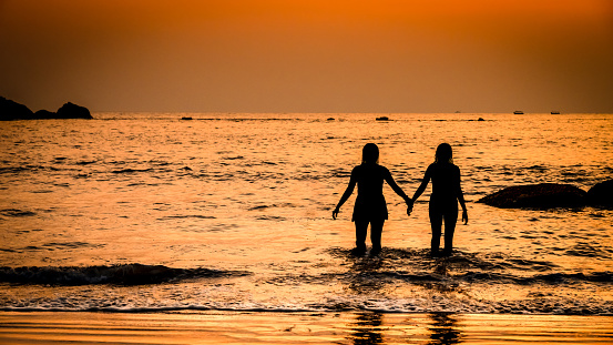 Photograph of two ladies holding hands as they witness the sunset. Love is in the air without boundaries of sex, race, religion and culture.