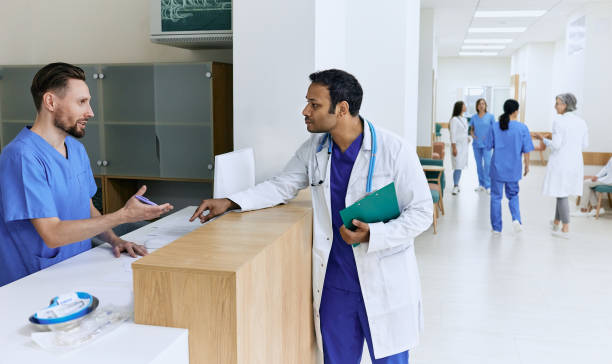 istock Medical assistant on duty talking with Indian doctor while working day standing near reception desk at lobby of hospital 1441379407