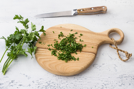 Wooden board with chopped parsley, a bunch of fresh parsley, a knife on a light blue background, top view. Cooking delicious homemade food