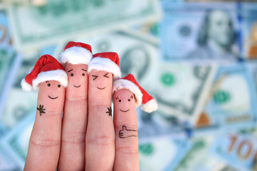 Fingers art of friends celebrates Christmas on the background of money. The concept of a group of people laughing in new year hats.