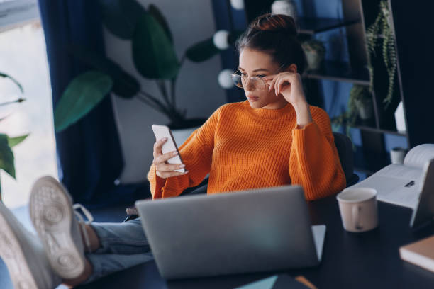 istock Confident young woman holding her feet on desk while using smart phone in office 1441382503