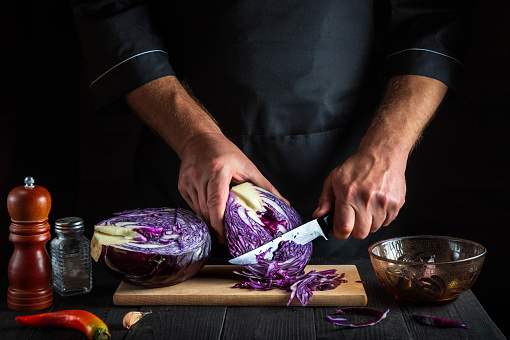 Cook cuts red cabbage with a knife. Cooking vegetable salad in the restaurant kitchen. Vegetable diet idea.
