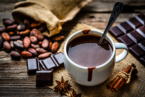 Sweet food: high angle view of a hot chocolate mug shot on rustic wooden table. Cocoa beans, dark chocolate bar and pieces and a spoon filled with chocolate powder complete the composition. High resolution 42Mp studio digital capture taken with Sony A7rII and Sony FE 90mm f2.8 macro G OSS lens