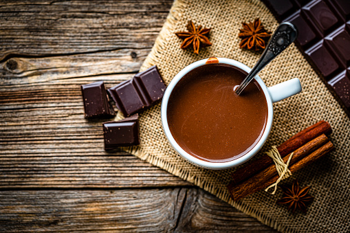 Sweet food: high angle view of a hot chocolate mug shot on rustic wooden table. Cinnamon sticks, star anise and dark chocolate bar complete the composition. High resolution 42Mp studio digital capture taken with Sony A7rII and Sony FE 90mm f2.8 macro G OSS lens